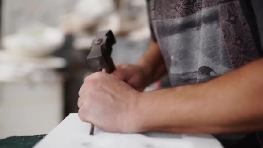A male taps on a thin chisel with a hammer as he makes a carving