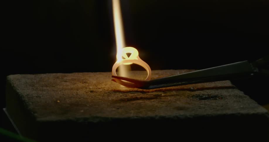 A flame heats a ring shaped piece of metal as a craftsman shapes it