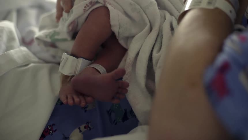A newborn baby with tiny feet is held by its mother at the hospital