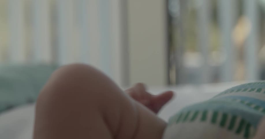 Infant lays in a crib, flexing fingers and toes