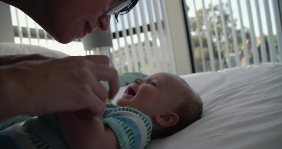A woman plays with a baby on a bed