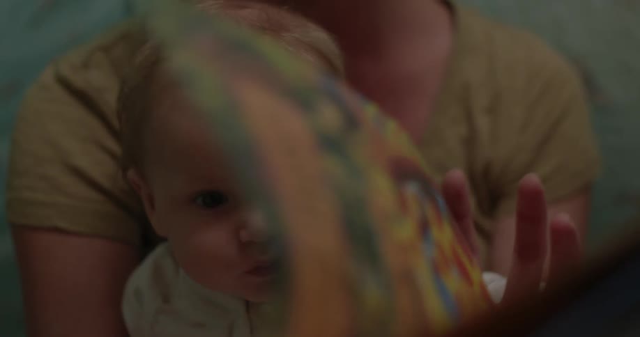 A parent is holding a baby who is flipping through a book