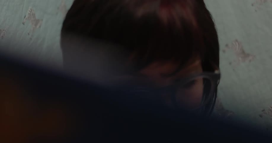 A woman is sitting on a bed in a room looking down and then up