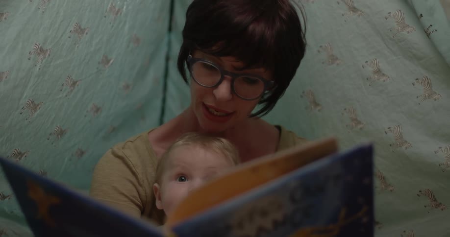 A woman wearing glasses reads a book to a baby