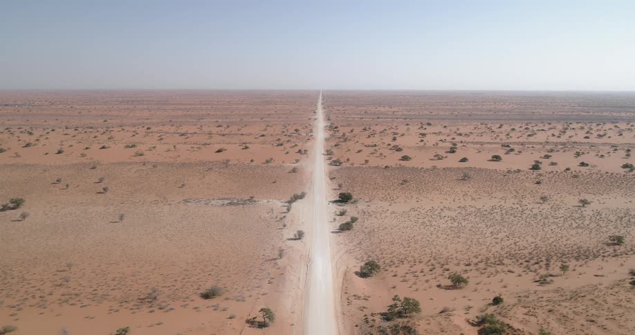 A narrow gravel road runs through a vast desert