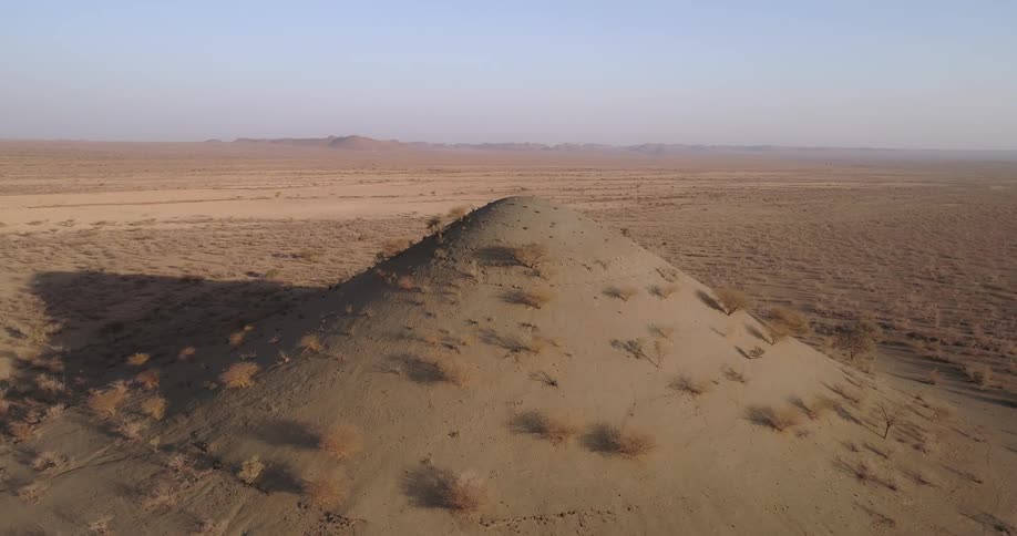 A large sand hill rises above the desert floor