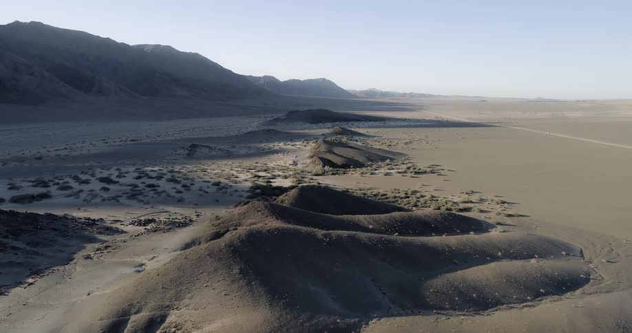 Sand dunes form in the desert near mountains