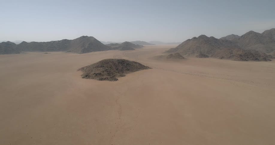 A dirt road runs through the desert near small hills and peaks