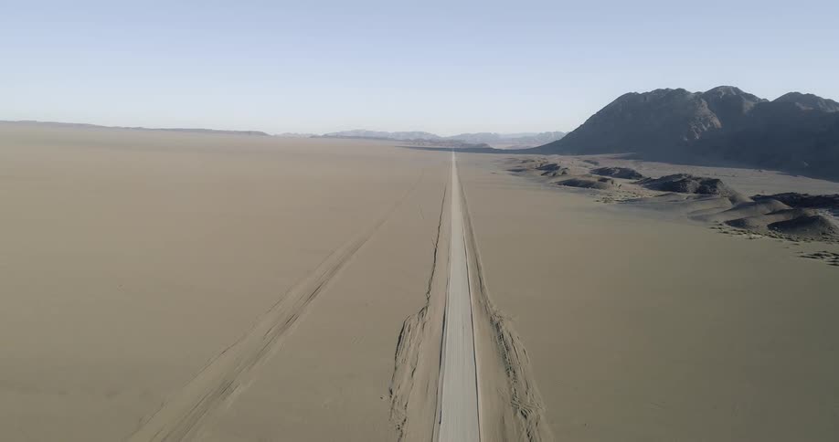 A road stretches through the middle of the desert with mountains to one side
