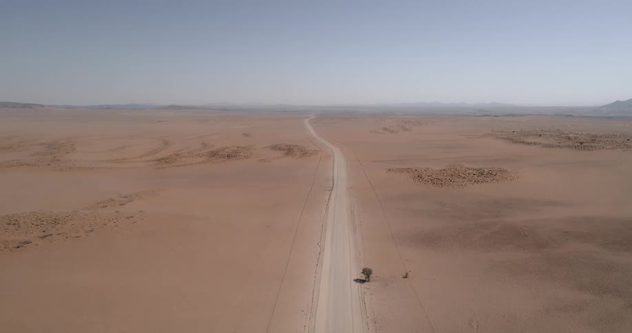 A narrow dirt road runs through the vast desert