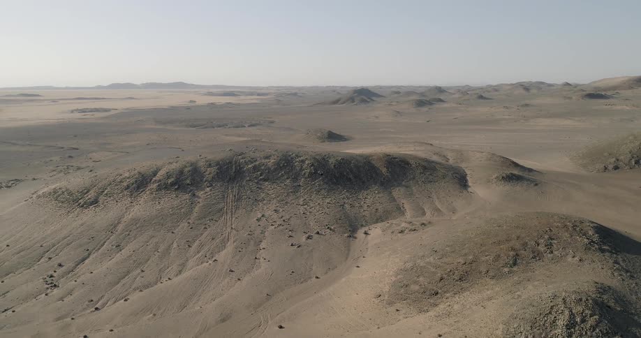 An aerial view shows a sprawling desert landscape with numerous hills and sand