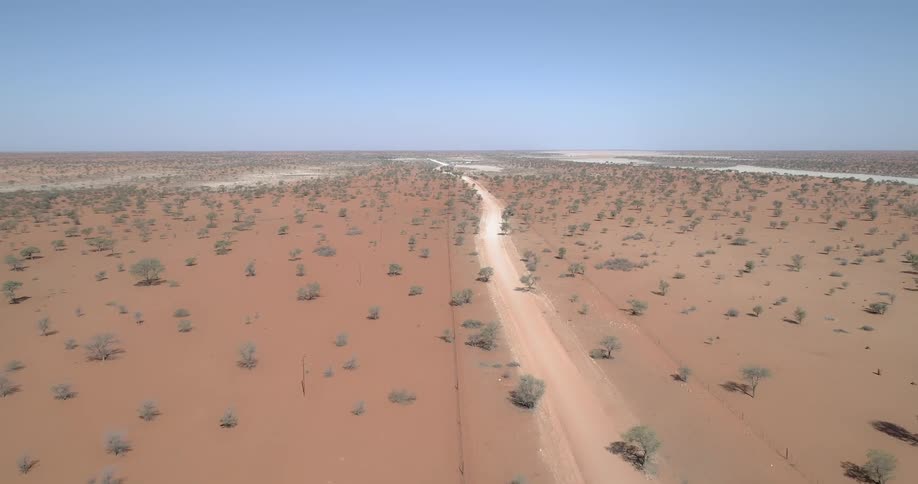 A long dirt road runs through the middle of a dusty desert landscape