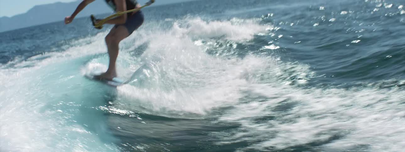 A man surfboarding tied to the back of a boat