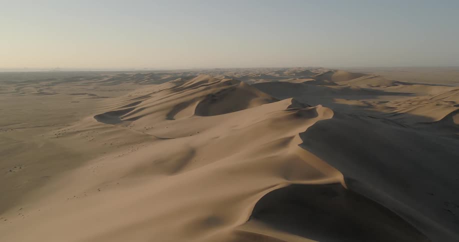 An aerial view of an expansive desert shows sand and series of dunes stretching to the horizon