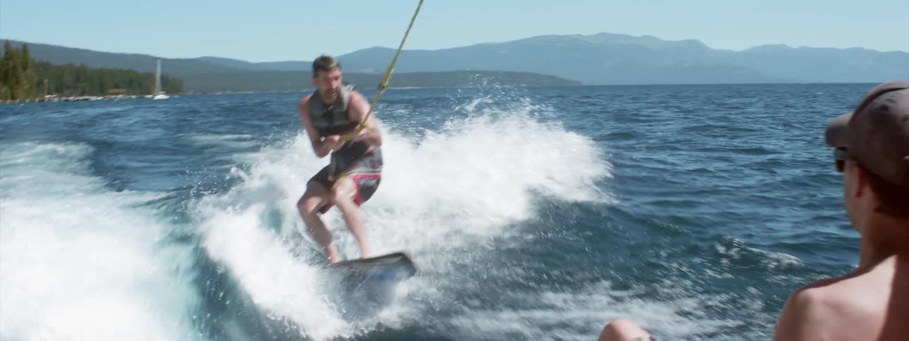 A man on a wake board being pulled by a motor boat nervously clutches the tow line and struggles to stay upright