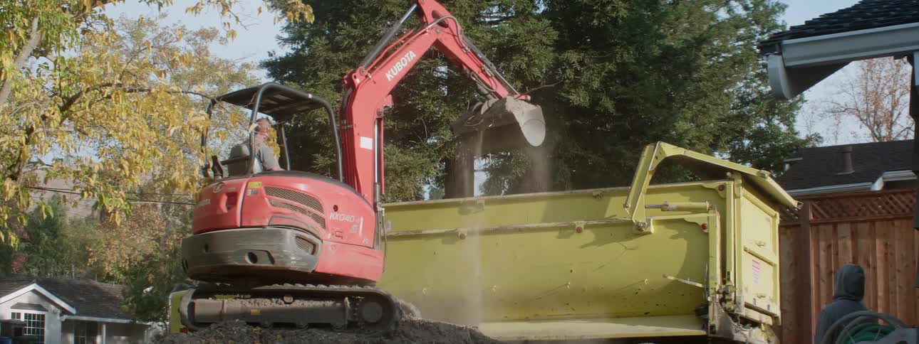 A truck places dirt into the back of a dump truck