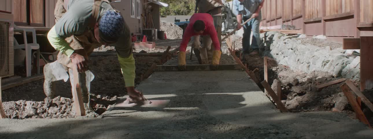 Several workers are laying concrete in forms for a sidewalk