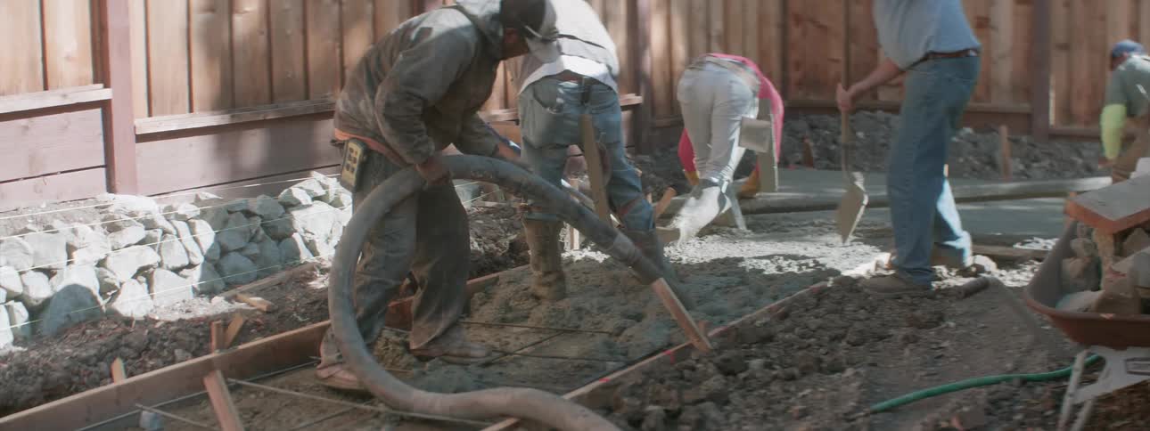 A group of construction workers lay cement into a large mold