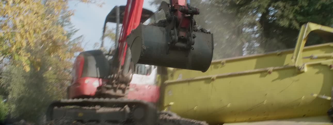A backhoe scoops dirt from a dirt pile and places it in a truck