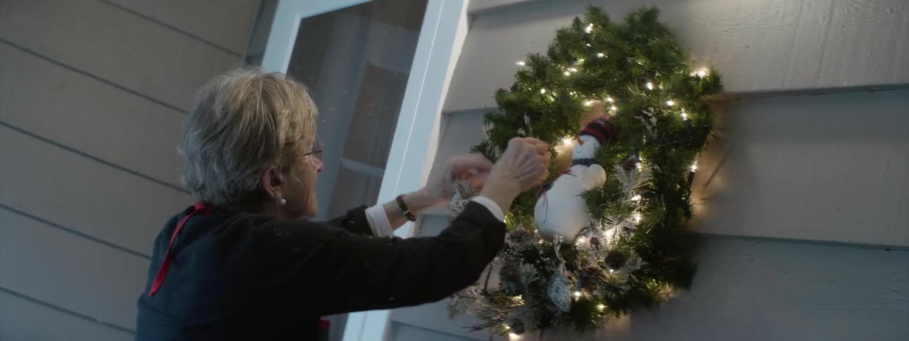 A woman hanging up a christmas wreath outside her home