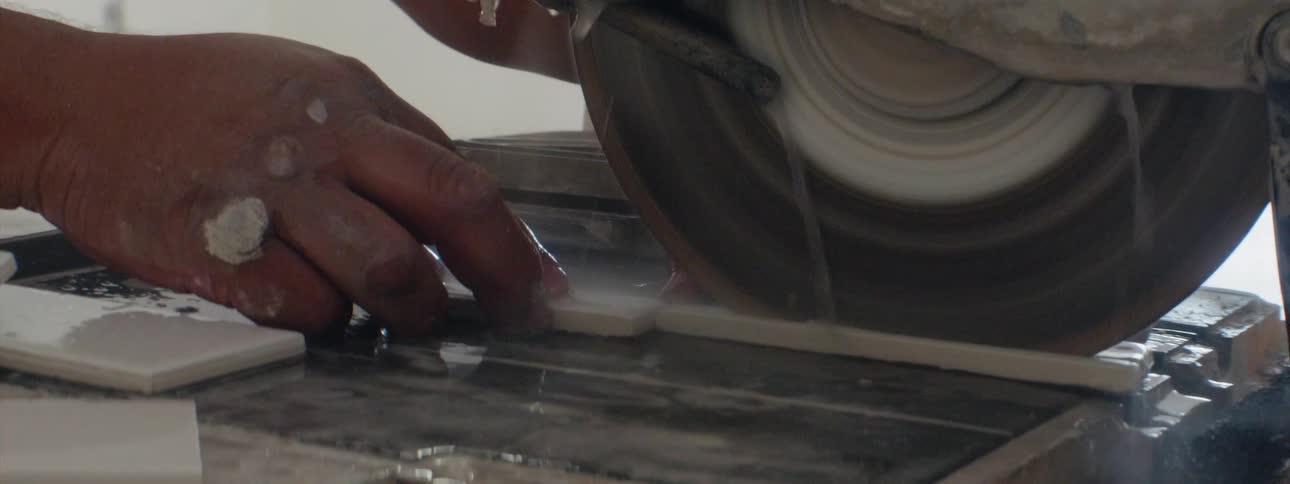 A man is cutting a thin piece of tile on a tile saw