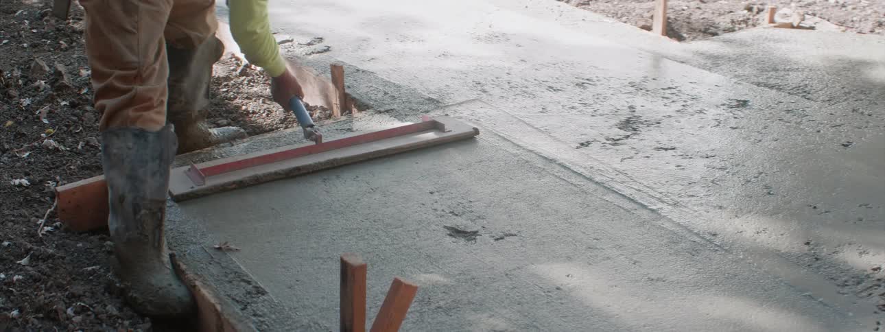 A construction worker uses a push style level to smooth out concrete