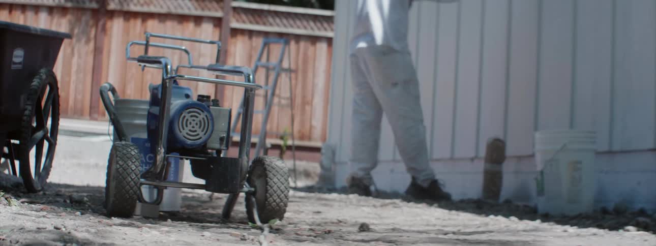 A man is using a paint sprayer to paint the outside of a building white