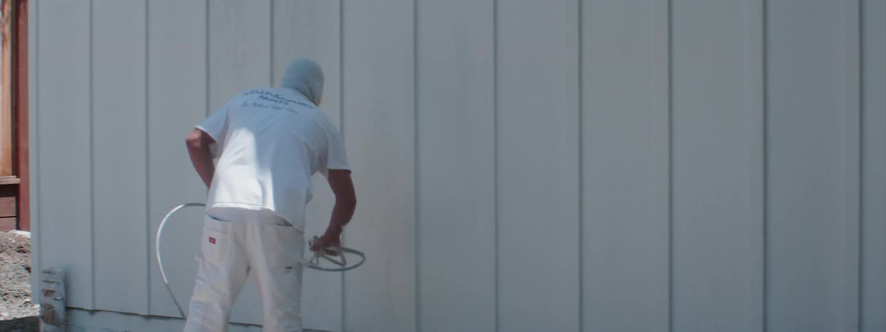 A worker spray paints siding white