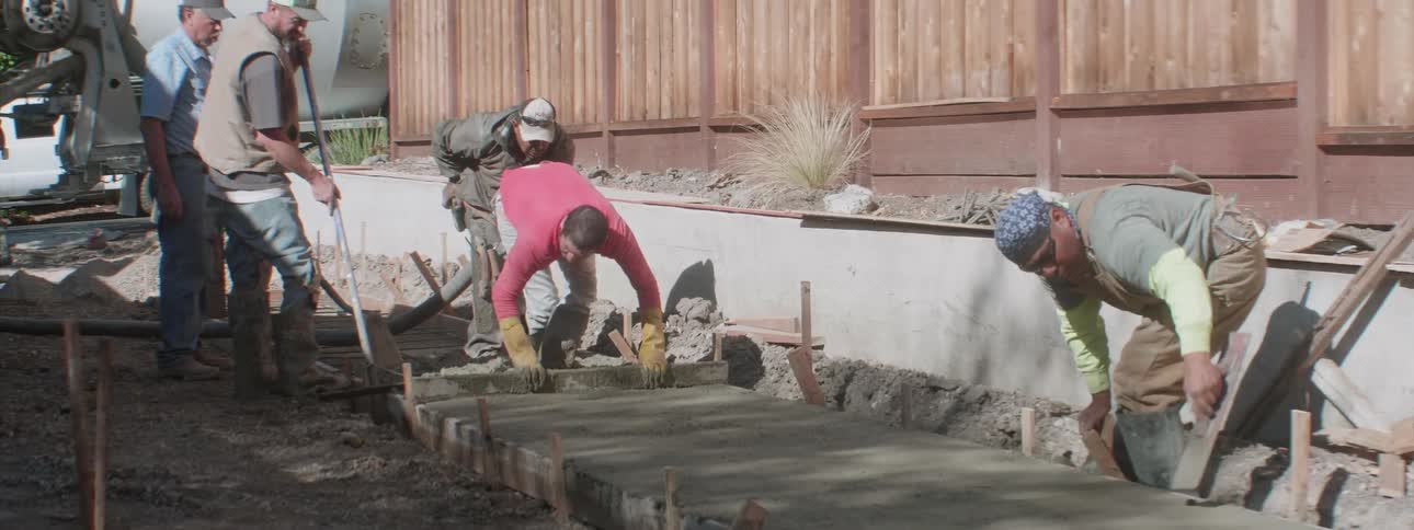 Construction workers smooth out cement as they build a sidewalk