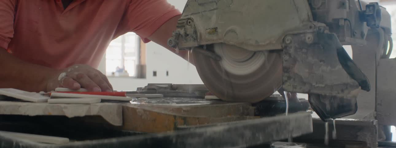 A man pushes the guide forward as water drips from the tile saw