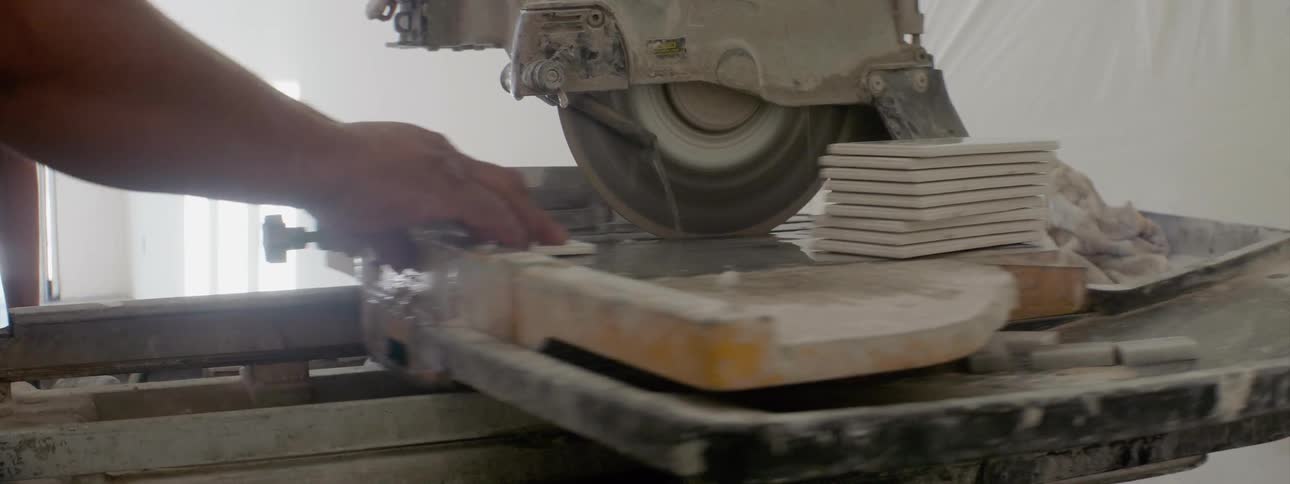 A worker stacks and cuts tiles with a saw