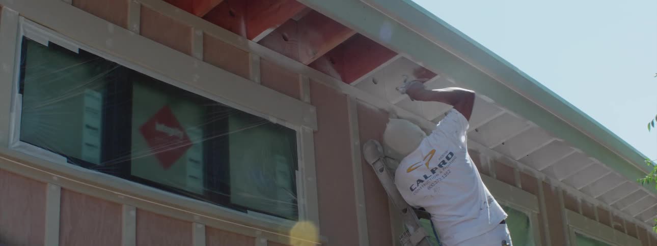A man paints the underside of a porch roof