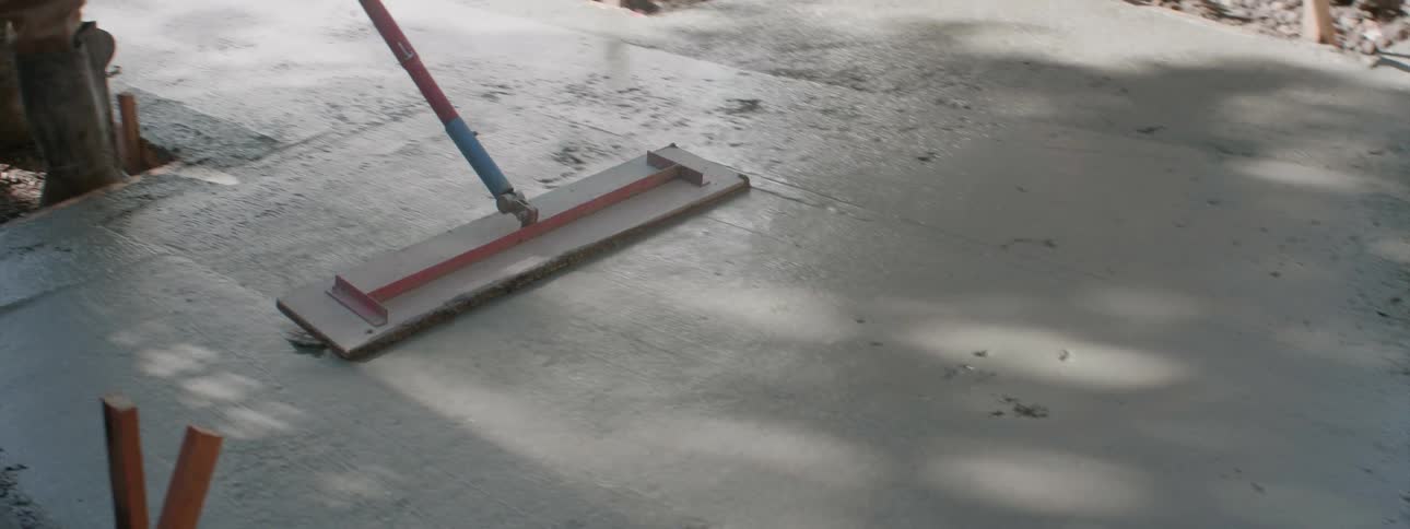 A worker smooths freshly poured concrete on a sidewalk