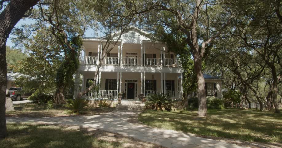 A large two story plantation style house is situated amidst several tall trees