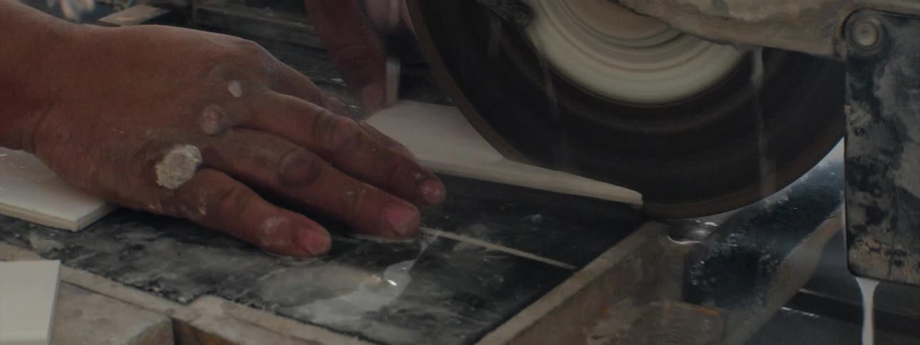 A man is cutting a piece of white ceramic tile on a tile saw