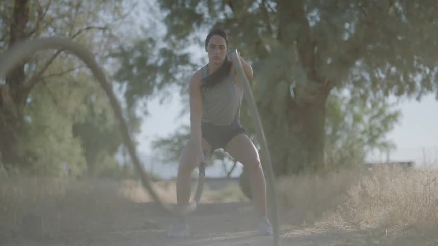 Female working out with battle ropes outdoors on dirt