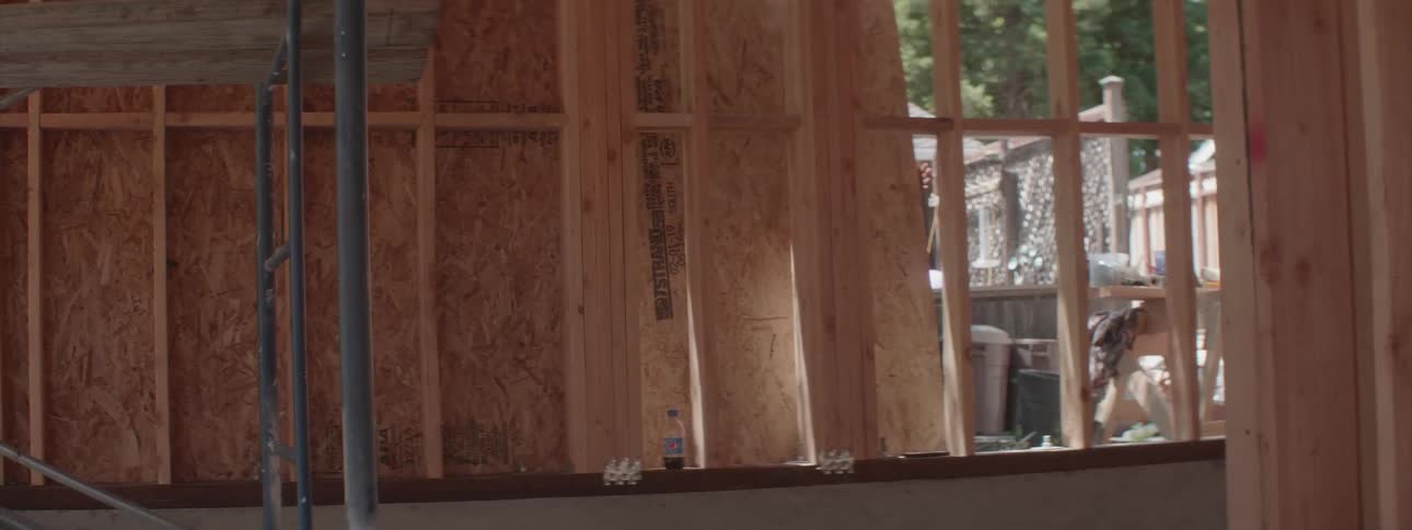 A person attaches plywood to the outside of a framed building