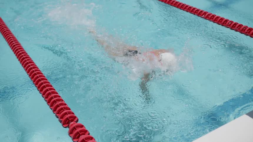 A female swims down a lane in a pool before flipping underwater and pushing off the wall to change direction