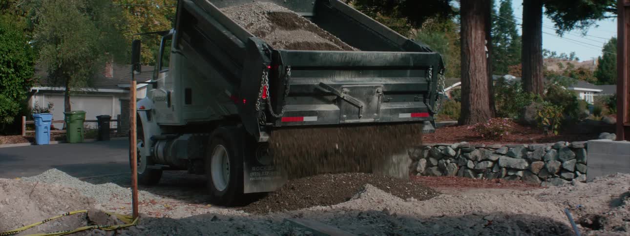 A dump truck is dumping a load of soil onto a property