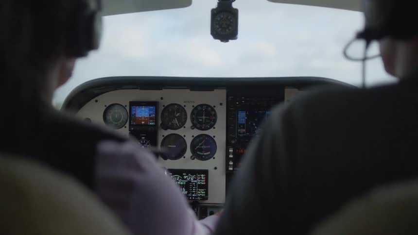 Two people sit in the cockpit of a small propeller airplane that is flying