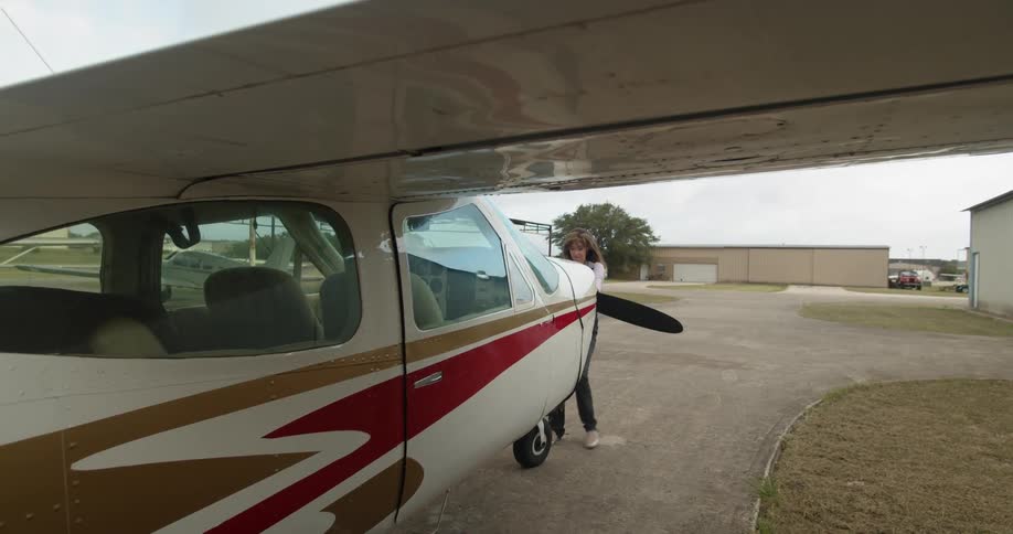 A woman pulls on the propeller of a small airplane that is grounded at an airfield