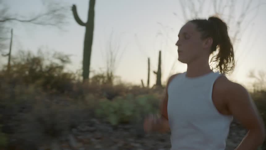 A woman jogs on a road past cactus trees and brush at sunset