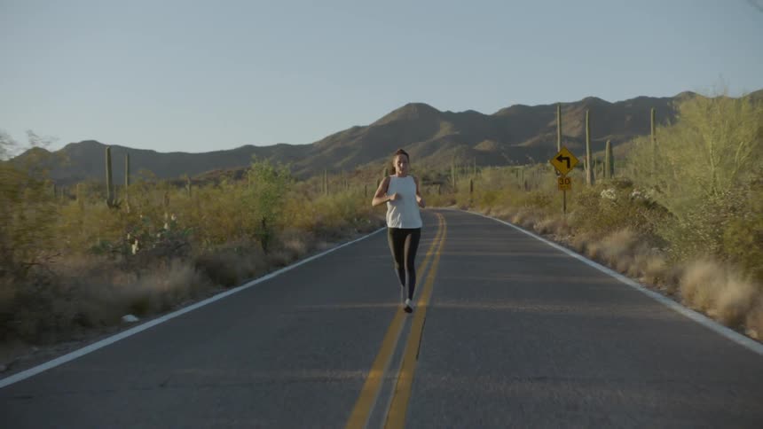 Woman runs on the asphalt road in the countryside during day time