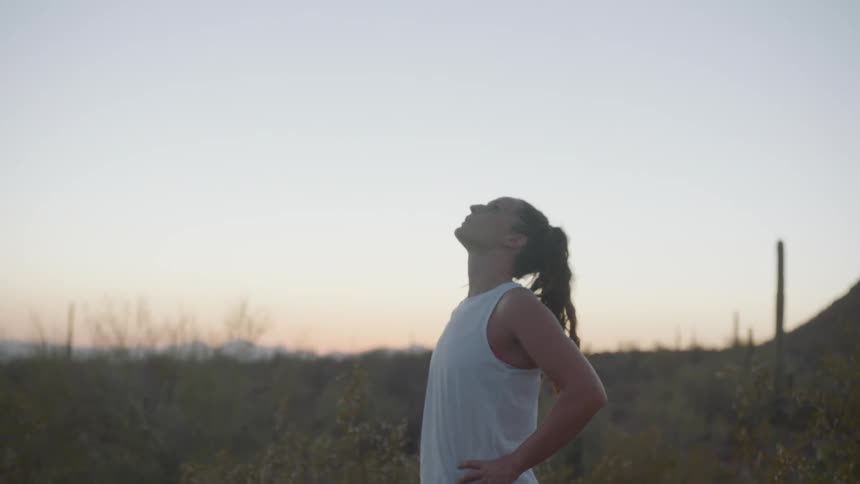 Woman with pony tail looks up and takes a deep breath outdoors at dusk