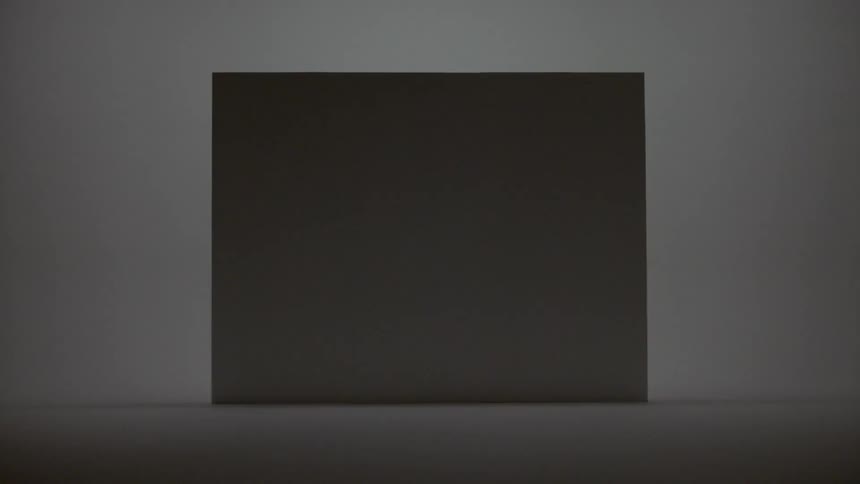 In a dimly lit room a rectangular screen is hung against a featureless wall