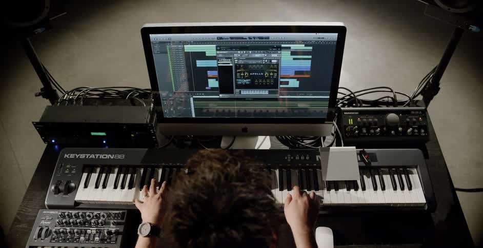 A man sitting before a monitor playing a musical keyboard