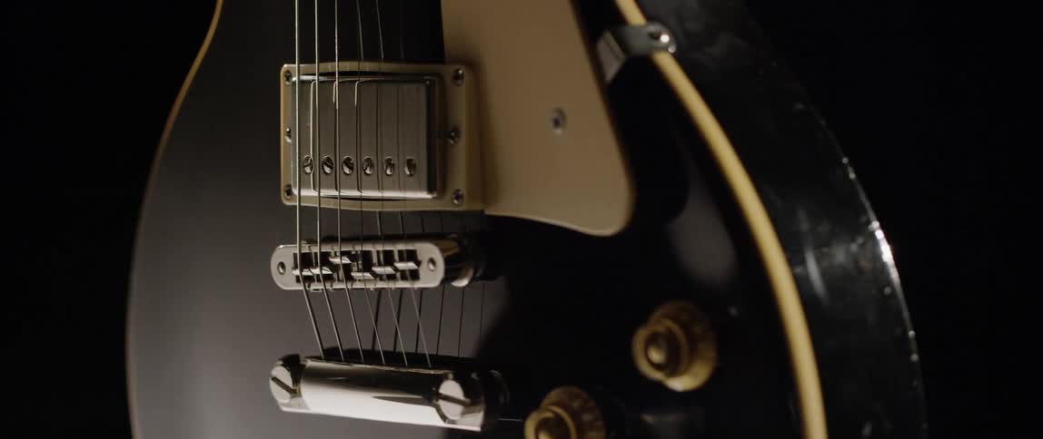 A small black guitar spinning slowly in a dark studio