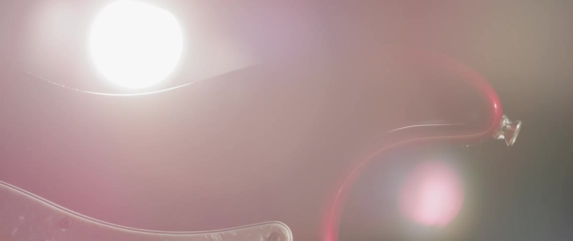 A bright light shines behind a close up of a guitar