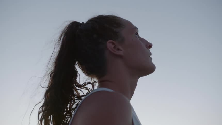 A female athlete looks up at the sky then back down as she catches her breath