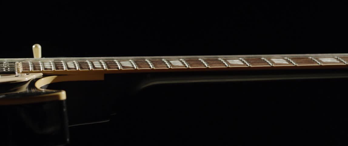An ivory electric guitar is resting on a flat black surface